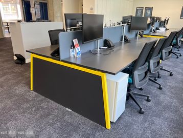 Used bench desks with charcoal grey tops and yellow splayed legs. 